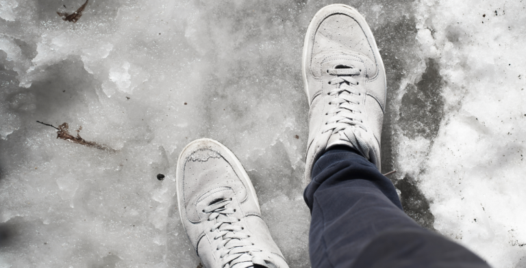 Two sneakered feet on melting snow.