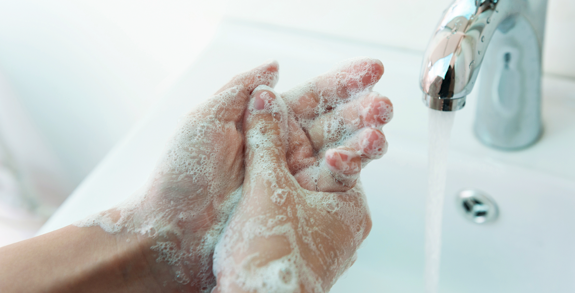 Close up of sudsy hands and running water in a sink.