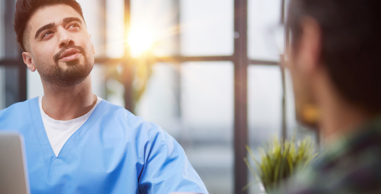 A man in scrubs sitting in front of a laptop.