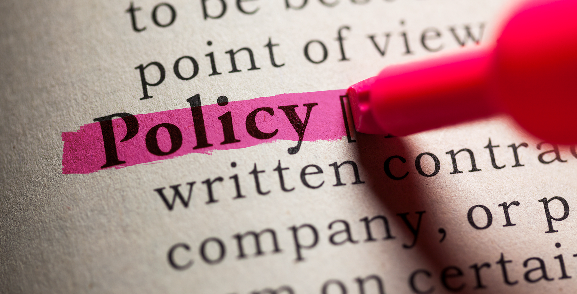 A pink marker is highlighting the word policy in a book.