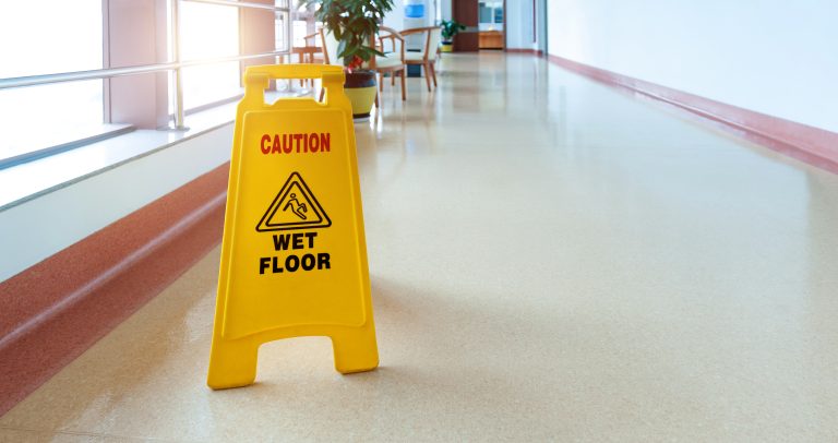 Yellow Cau8tion Wet Floor sandwich board sign in a hospital hallway.